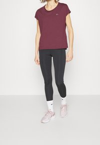 Mörkröd kortärmad t-shirt med rundad halsringning och liten logotyp, kombinerad med svarta leggings och ljusrosa träningsskor.