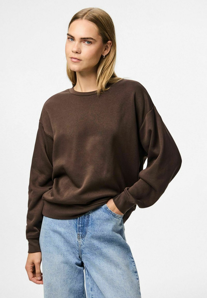 Sudadera marrón de gran tamaño con cuello redondo y mangas largas, combinada con jeans de color azul claro, que presentan un ajuste relajado y una textura suave.