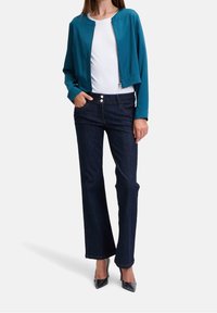 Teal cropped jacket over a white top, paired with dark blue high-waisted jeans. The jeans feature two button details and a straight cut.