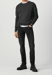 Tmavě šedý pletený svetr s žebrovými manžetami, navlečený přes bílou tričko. Úzké černé džíny a černé šněrovací boty.