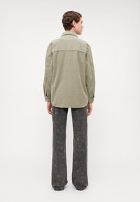 Chemise en velours côtelé vert olive avec col, manches longues et ourlet arrondi. Associée à un pantalon évasé gris avec un motif d'étoiles.