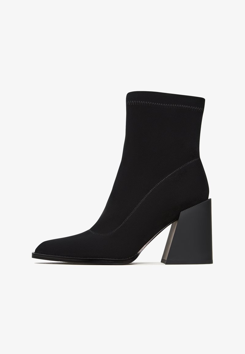 Botín negro de tobillo hecho de tela suave, con punta afilada, tacón ancho alto y detalles de costura en contraste. Diseño elegante y minimalista.