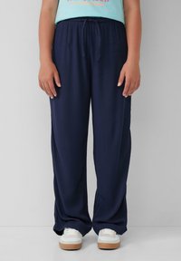 Marineblaue, locker sitzende Hose aus strukturiertem Stoff mit elastischem Bund und Kordelzug. Kombiniert mit weißen Sneakers für einen Kontrast.