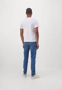 Weißes T-Shirt mit kurzen Ärmeln und Rundhalsausschnitt, kombiniert mit blauen Jeans und beigen Sneakers, von hinten betrachtet.