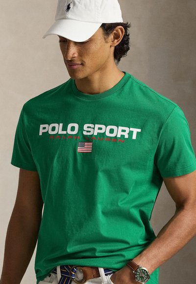 Žalia medvilninė marškinėliai su spauda „POLO SPORT“ ir „Ralph Lauren“ baltais ir raudonais rašmenimis, su maža Amerikos vėliava. Apvalus kaklas, trumpomis rankovėmis.