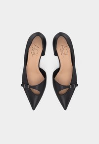 Μαύρα δερμάτινα φλατ παπούτσια μυτερά στη μύτη με λουράκι και μικρή αγκράφα, μπεζ εσωτερικά με ετικέτα "AGL", τοποθετημένα δίπλα δίπλα σε λευκό φόντο.