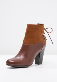 Bottine marron avec un bout en cuir lisse et une tige en daim doux, ornée de détails en dentelle et dotée d'un talon empilé pour un peu plus de hauteur.