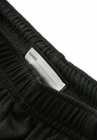 Shorts neri con elastico in vita realizzati in un tessuto testurizzato. Un'etichetta bianca cucita nella vita riporta "NOME..." con delle linee tratteggiate sottostanti.