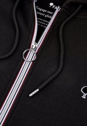 Felpa nera con zip, con strisce di accento bianche e rosse, hardware della zip in argento e un piccolo logo a forma di albero bianco sul petto. Tessuto morbido.