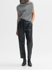 Szary, prążkowany, bezrękawnikowy golf w połączeniu z czarnymi spodniami z faux skóry z troczkiem i czarnymi botkami za kostkę. Minimalistyczny fason.