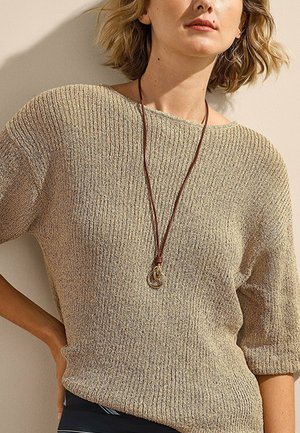 Woman wearing a beige textured knit sweater with half sleeves and a long leather necklace with gold rings pendant.