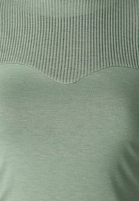 Grøn top med en scallop-design, hvor den øverste del har en lysere ribbet tekstur, mens den nederste del har en glat finish.