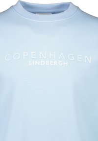 Ljusblå sweatshirt med rundad halsringning, med präglad text "KOPENHAMN" och "LINDBERGH" på framsidan. Slät textur.