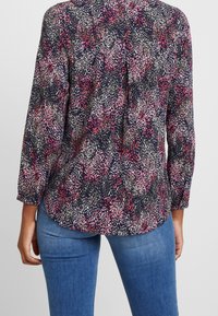 Bluse mit Blumenmuster in Marineblau mit Farbtönen von Pink und Grün. Hat lange Ärmel und einen abgerundeten Saum, hergestellt aus leichtem Stoff.
