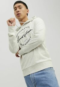 Lys grå hættetrøje med snøring, der har sort grafisk tekst og en afslappet pasform, parret med blå jeans.