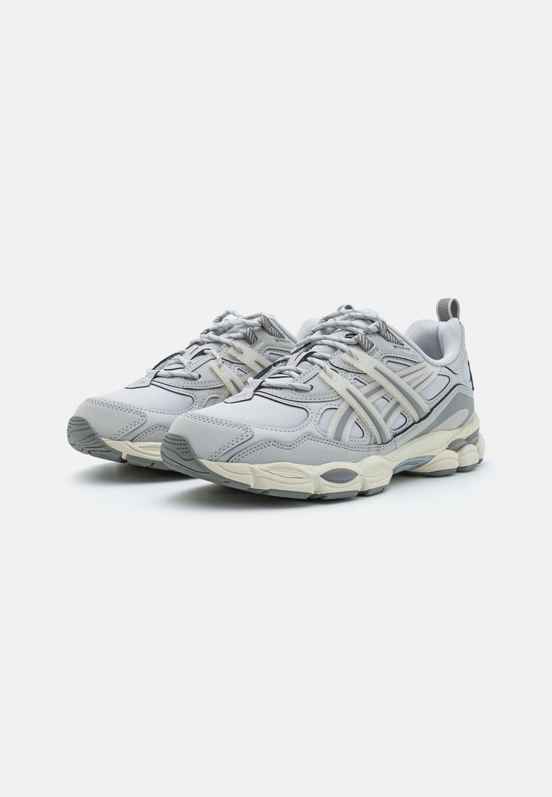 Sportliche Sneaker aus hellgrauem Leder mit Mesh-Akzenten, ausgestattet mit einer strukturierten Gummisohle und geschichteten Designelementen. Subtile schwarze Details.