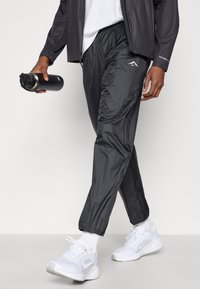 Μαύρο, ελαφρύ αθλητικό παντελόνι με ελαστική μέση και μανσέτες, σε συνδυασμό με άσπρα αθλητικά παπούτσια και μια μαύρη μπουκάλα νερού.