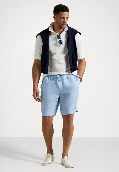 Light blue linen shorts with elastic waistband, paired with a white collared polo shirt and a navy cable-knit vest. White sneakers complete the look.