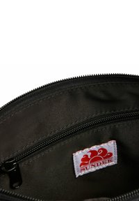 Interno di una borsa in tessuto nero, con fodera texturizzata, dotata di una cerniera e un'etichetta bianca con un logo a onda rossa, che mostra il nome del marchio "SUNDEK."