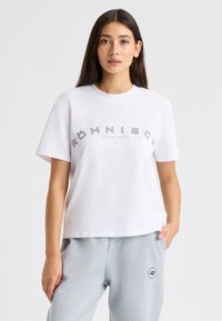 Camiseta de algod�ón blanca con cuello redondo y mangas cortas, con "Röhnisch Sportswear desde 1945" impreso en texto gris en el pecho.
