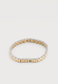 Δίχρωμο μεταλλικό βραχιόλι με χρυσούς κεντρικούς κρίκους και ασημένιες άκρες, με μικρό πράσινο λογότυπο κροκοδείλου σε έναν χρυσό κρίκο.