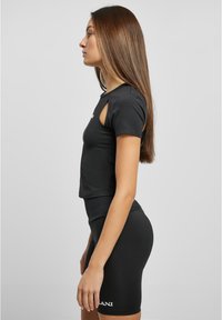 Zwarte sportieve tweedelige set bestaande uit een cropped top met korte mouwen en uitsnijdingen, en hoge fietsbroeken. Glad textuur, slim fit ontwerp.