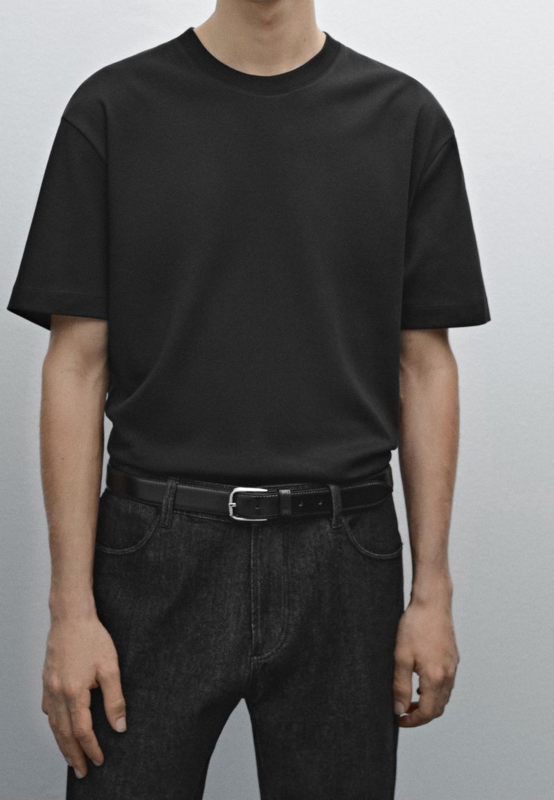 T-shirt noir à manches courtes en tissu lisse, associé à un jean denim foncé et une ceinture noire avec une boucle en argent. Design simple et ajusté.