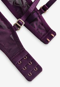 Bretea de sutien mov închis cu textură de plasă și satin, prevăzută cu accesorii reglabile și închidere cu mai multe cârlige pentru ajustarea mărimii.