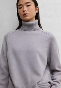 Suéter de cuello alto gris claro hecho de un suave tejido de punto, con puños y cuello acanalados, y un corte holgado con detalles de costura mínimos.