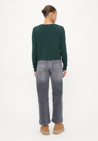 Grønn kortermet genser, grå vide jeans og brune plattformstøvler. Genseren har lange ermer; jeansene har baklommer og en falmet finish.