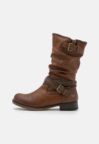 Botte en cuir marron mi-mollet avec un design décontracté, accent de sangle et clous décoratifs en métal. Elle présente une pointe arrondie et un petit talon empilé.