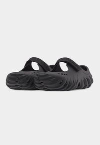 Paire de sabots noirs à enfiler avec des sangles réglables et des semelles texturées et ventilées sur un fond blanc uni.