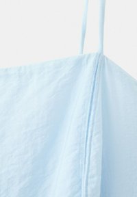 Tissu bleu clair avec une fine bretelle et un détail visible de couture verticale sur un fond blanc uni.