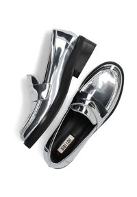 Zilveren metallic loafers met een glanzende afwerking, zwarte rubberen zool en een decoratieve band aan de voorkant. Label: Bibi Lou.