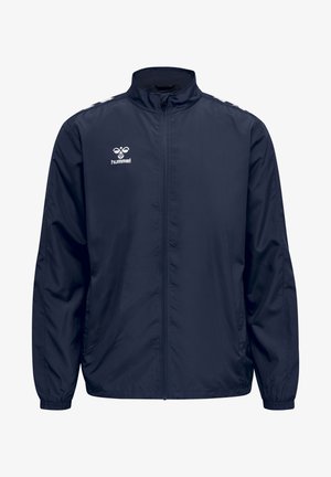 Veste de sport bleu marine avec fermeture éclair à l'avant, poignets élastiques et logo blanc ; conçue dans un tissu lisse et léger, avec des détails minimalistes.