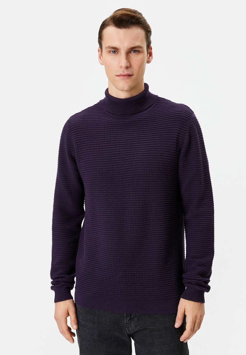 Lila Rollkragenpullover aus strukturiertem Strickstoff, mit langen Ärmeln und gerippten Bündchen. Getragen mit dunklen Jeans.