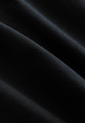 Schwarzer Stoff mit glatter Textur, der subtile Lichtreflexionen und einen leichten Glanz aufweist, mit weichen, fließenden Falten.