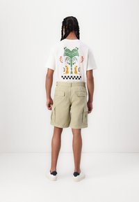White t-shirt with colorful palm tree and animal print on back, paired with light olive cargo shorts featuring side pockets. White sneakers.