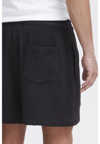 Black shorts made of textured fabric with a quilted pattern and elastic waistband. Features a single patch pocket on the back.