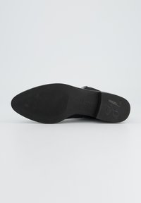 Semelle de chaussure noire avec une forme pointue, texture rainurée pour une meilleure adhérence et une marque contrastante. Fini lisse avec des détails minimaux.