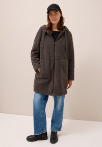 Manteau zippé à capuche en polaire gris anthracite, confortable, avec deux poches avant, associé à un jean bleu clair et des bottes en cuir à lacets noires.