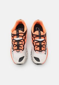 Baskets de course en mesh blanches avec des accents noirs et orange, présentant des lacets noirs, une semelle texturée et une marque visible sur le côté.