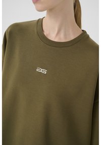 Olijfgroene sweatshirt gemaakt van zachte stof, met een ronde hals en een klein geborduurd logo in het wit op de borst.