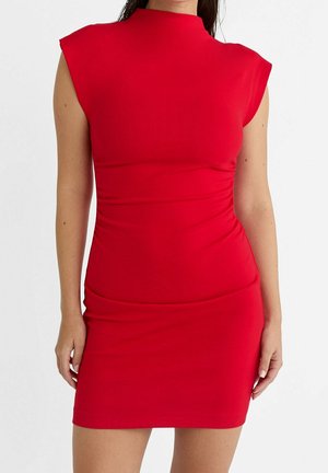 Woman wearing sleeveless, fitted red dress with shoulder pads and high neckline, standing with arms relaxed by sides.