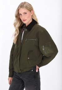 Olivgrüne Bomberjacke mit einem Cordkragen, mehreren Reißverschlusstaschen, elastischem Bund und einem lockeren Schnitt.