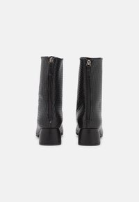 Bottines noires avec un motif crocodile texturé, dotées d'une fermeture éclair à l'arrière et d'un petit talon bloc. Matériel en cuir lisse.