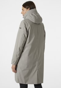Šedý voděodolný kabát s vysokým límcem a kapucí. Má dlouhé rukávy, rovný střih a decentní logo na rukávu. Texturovaná tkanina.