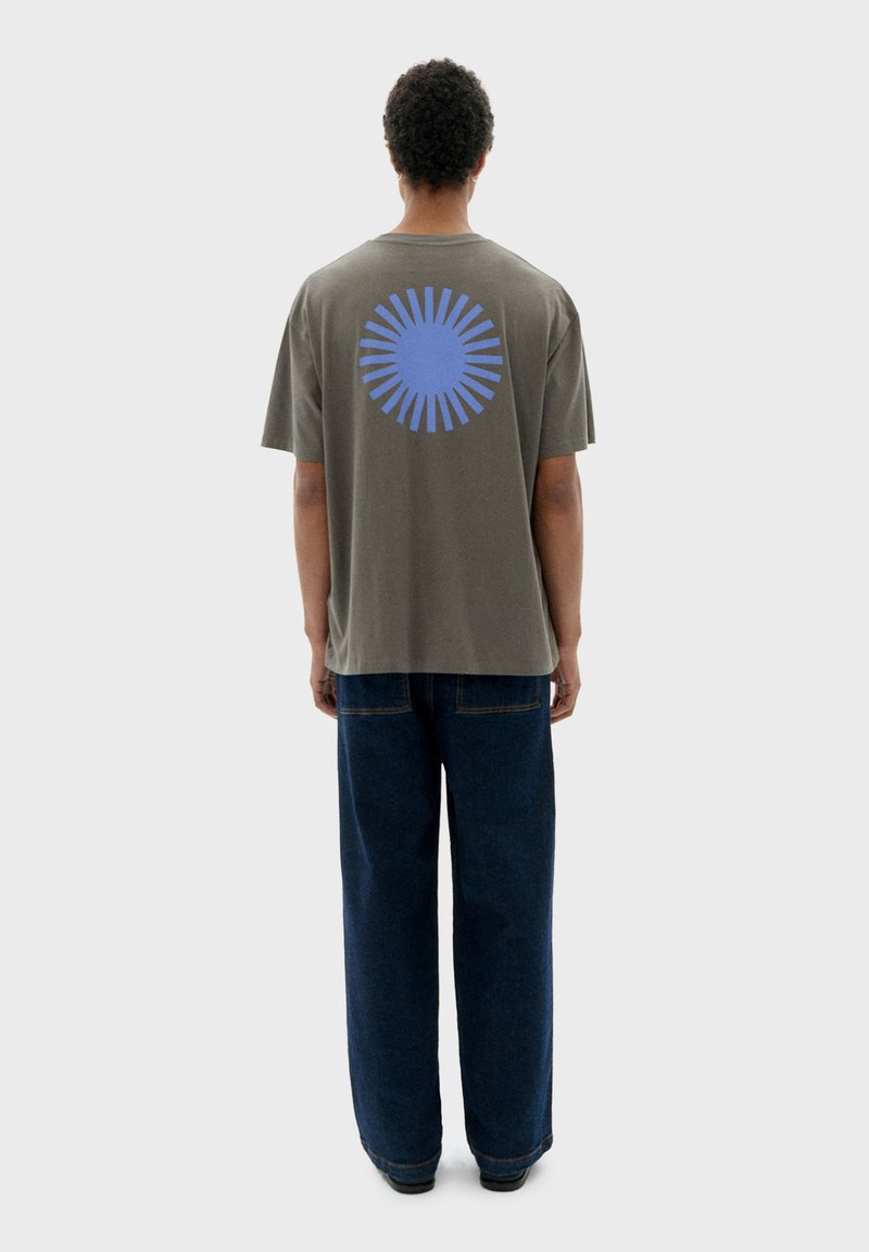 Grijs katoenen T-shirt met een blauwe zonnestraalgrafiek op de achterkant, gecombineerd met brede blauwe denim jeans.
