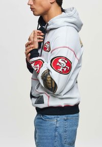 Herren-Grauer Hoodie mit San Francisco 49ers Logos, roten Akzenten, Kordelzugkapuze und schwarzen Bündchen. Verfügt über verschiedene sportliche Patches.