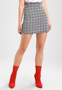Jupe mini à carreaux noir et blanc avec une taille froncée, associée à des bottines rouges éclatantes.